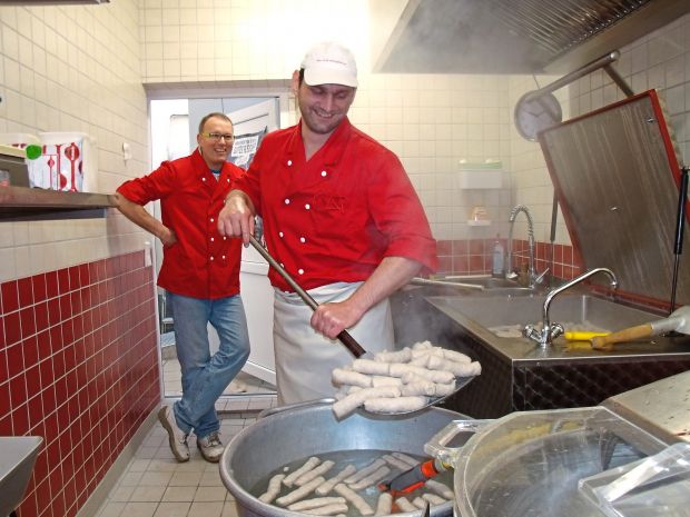 Nach dem Bad im heißen Wurstkessel kühlt Fleischer Stefan Gudjan die Currywürste ohne Darm sofort ab. Fleischermeister Jörg Oppen hat die handwerkliche Herstellungsweise im Blick. Nach dem Bad im heißen Wurstkessel kühlt Fleischer Stefan Gudjan die Currywürste ohne Darm sofort ab. Fleischermeister Jörg Oppen hat die handwerkliche Herstellungsweise im Blick.